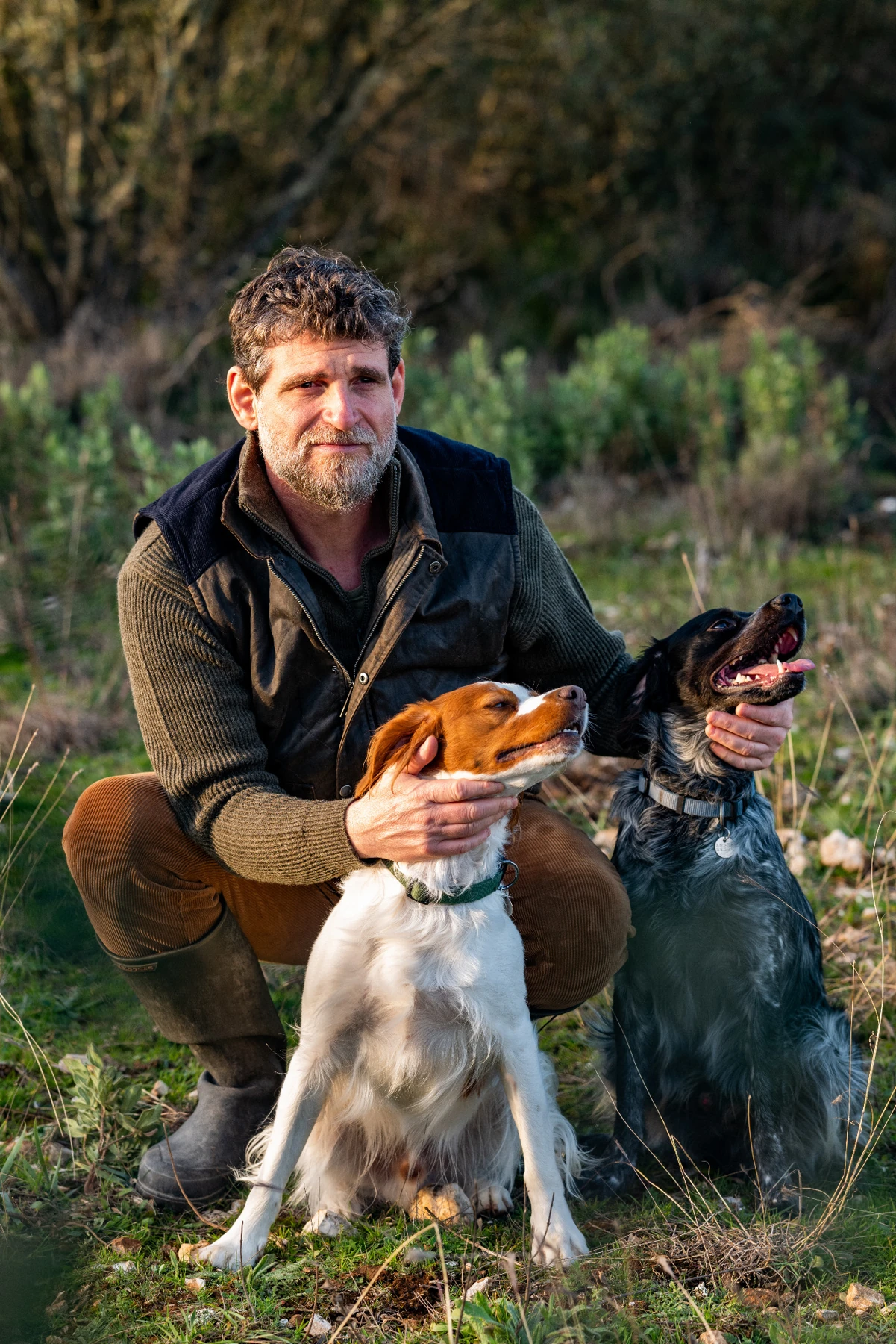 Richard sur Terre accroupi en extérieur avec deux chiens.